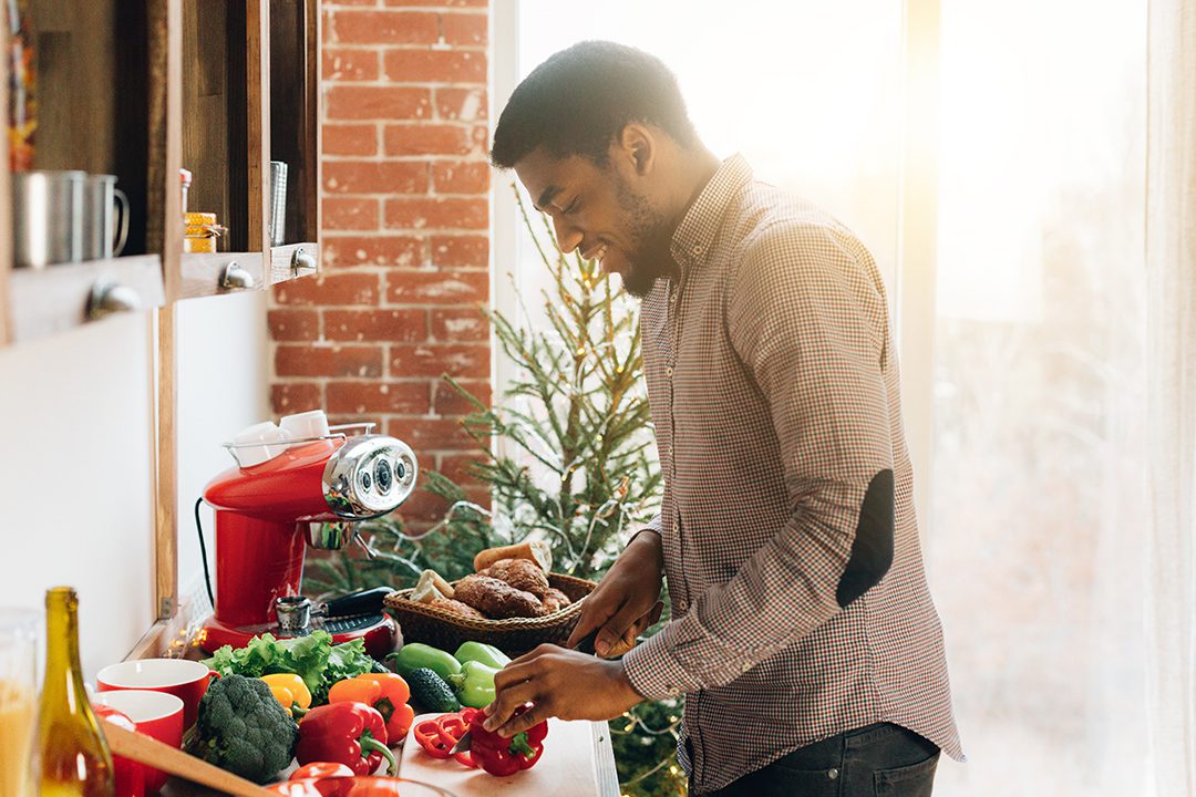 Vegetarian lifestyle. Cheerful african-american guy preparing healthy meal with fresh vegetables at kitchen